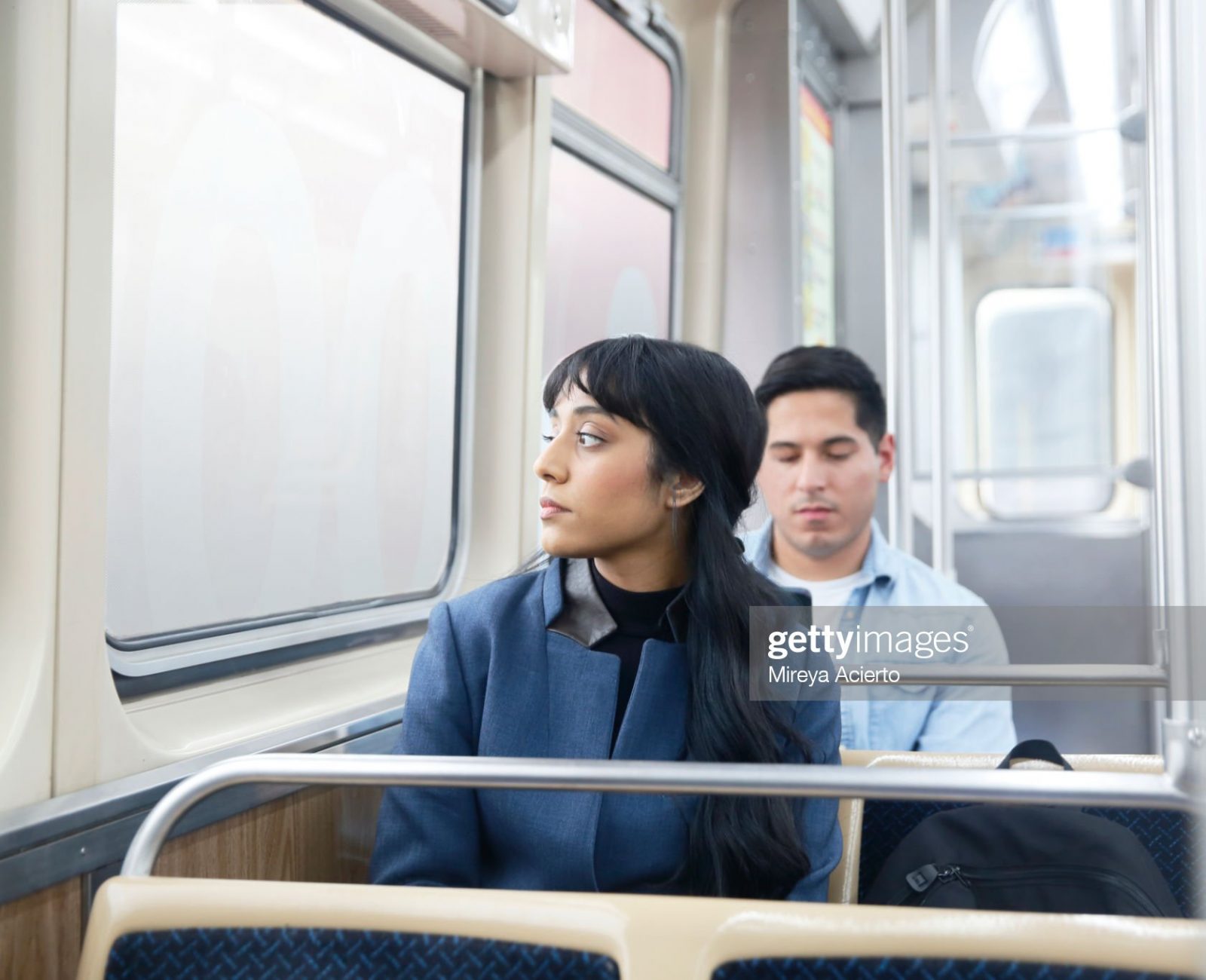 A LatinX male and female with long dark hair, sit on the subway train while wearing business casual clothing.